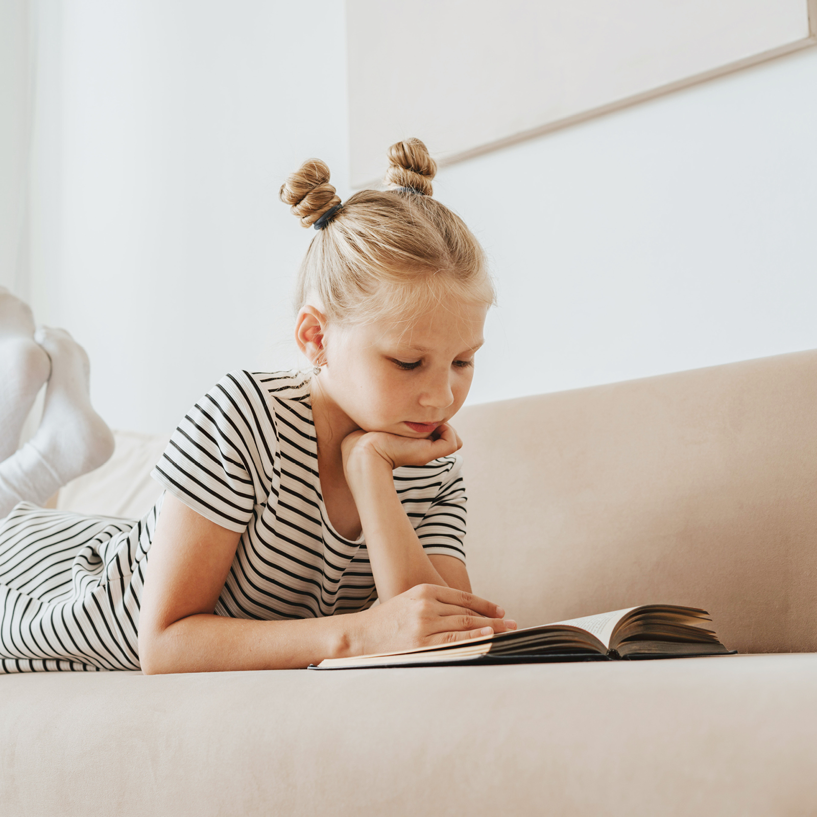 Mädchen liegt auf Sofa und liest ein Buch