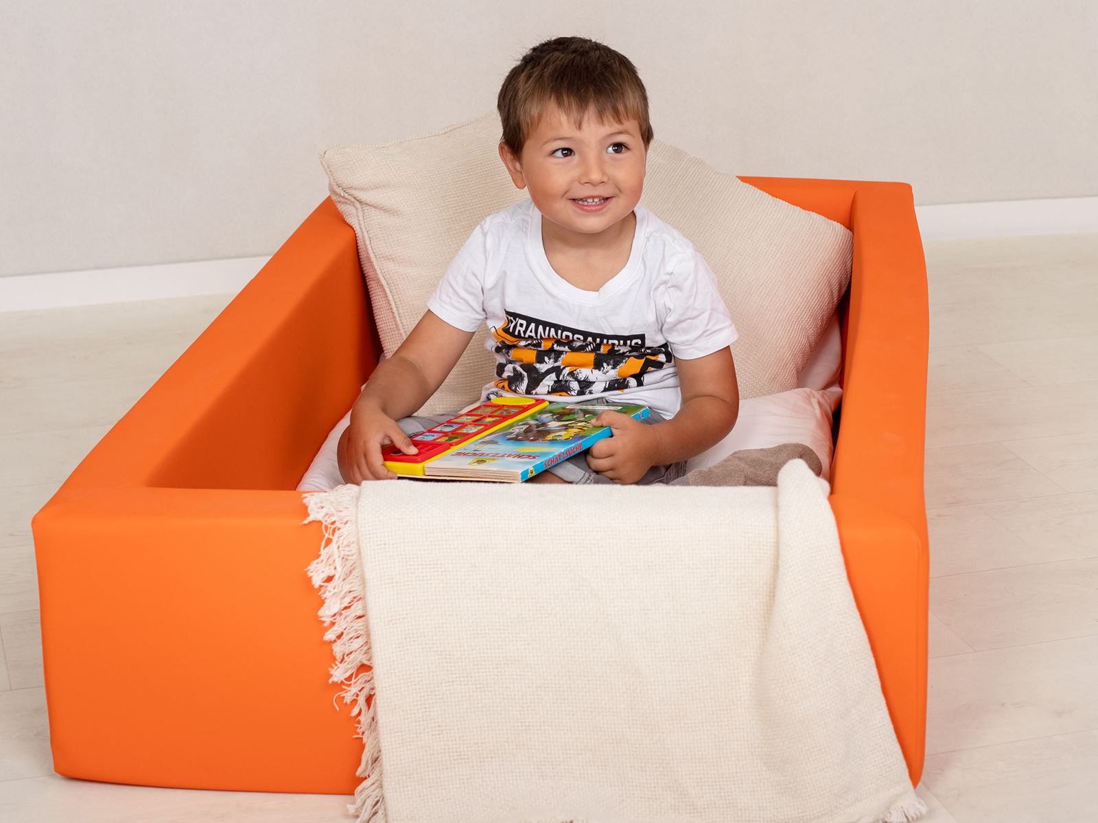 Weichschaumbetten aus liebevoller Handarbeit kleiner Junge sitzt in einem GEHLER Weichschaumbett in orange